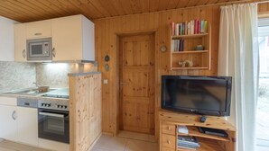 A compact kitchen with a microwave, oven, and wooden cabinets. - Doppelbungalow im Skandinavischen Stil mit Terrasse im Ferienpark Mirow (Mirow)