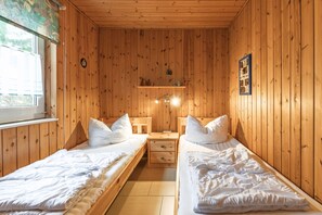 Ein Zimmer mit Holzwandverkleidung, zwei Einzelbetten, einem Nachttisch, einem Regal mit Gegenständen und einem Fenster.