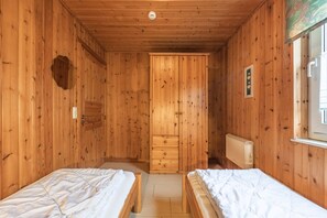 Een houten kamer met twee bedden, een radiator en een deur naar een andere kamer.