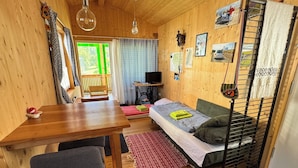Een houten interieur met een bed, een tafel, een stoel, een televisie en een raam met gordijnen.