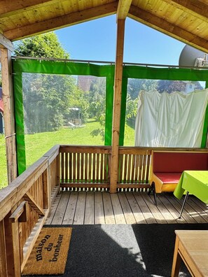 A covered outdoor area with a wooden deck, a bench, and a table with a green tablecloth. - Black Forest Homely Tiny House Casa Wendy (Loßburg)