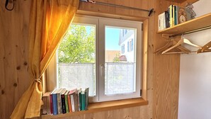 Een kamer met houten details, een raam met gordijn, een radiator en een boekenkast vol boeken.