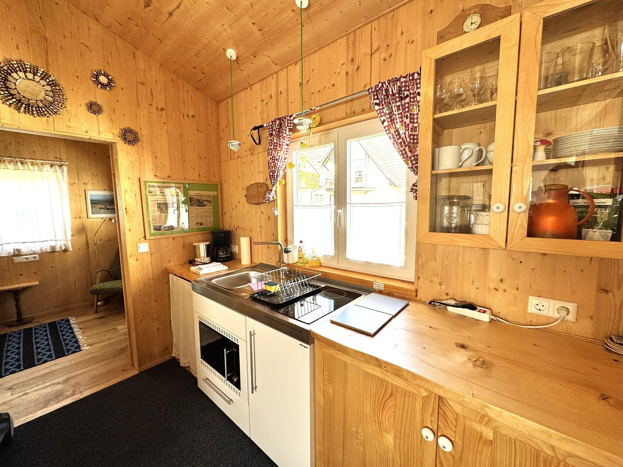 A wooden cabin interior with a kitchen, dining area, and a window with curtains.