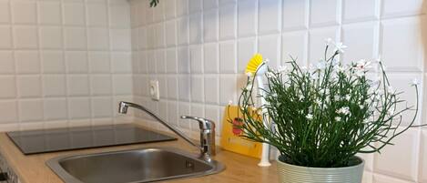 Una cocina con un lavamanos de acero inoxidable, una encimera de madera y una planta en maceta con flores blancas.