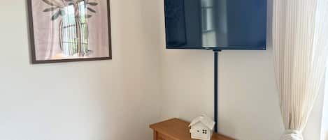 A flat-screen TV mounted on a wall, a wooden cabinet with drawers, and a framed artwork above the cabinet.
