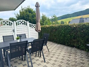 Eine Terrasse im Freien mit Tisch und Stühlen, einem Sonnenschirm und Blick auf eine grüne Landschaft.