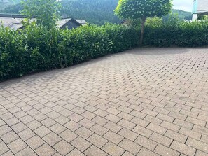 Ein gepflasterter Außenbereich mit einem geschwungenen Weg, umgeben von dichter Vegetation und einer Hecke.