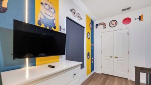 A room with a flat-screen TV on a white dresser, a door with a keyhole, and a wall clock. - THEMED 4 BR Coral Cay GEM w/Lake view-10 min to Disney-Free BBQ-Free resort (Kissimmee)