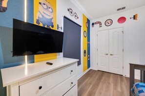 A room with a flat-screen TV on a white dresser, a door with a keyhole, and a wall clock. - THEMED 4 BR Coral Cay GEM w/Lake view-10 min to Disney-Free BBQ-Free resort (Kissimmee)