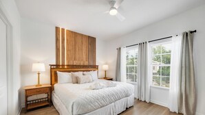 A hotel room with a large bed, two bedside tables, a ceiling fan, and a window with curtains. - THEMED 4 BR Coral Cay GEM w/Lake view-10 min to Disney-Free BBQ-Free resort (Kissimmee)