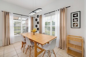 Un coin repas avec une table en bois, des chaises blanches, un vase de fleurs et un luminaire fixé au mur.