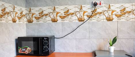 A microwave oven on a wooden countertop with a power cord plugged into a wall socket.