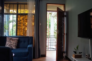 Una habitación con sofá azul, una puerta de madera que da al exterior y vistas a la vegetación.