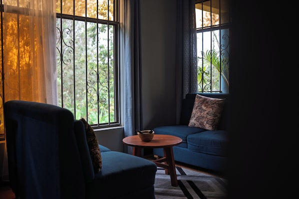 Una habitación con un sofá azul, una silla, una mesita redonda y una ventana con cortinas.