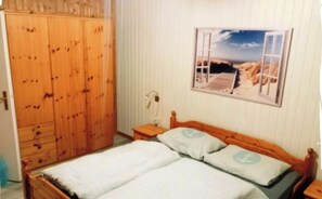 Ein Schlafzimmer mit Holzschrank, Bett mit zwei Kissen, Nachttisch und einem an der Wand hängenden Bild.