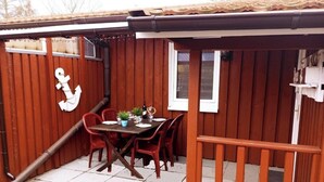 A wooden outdoor dining area with a table and chairs, a potted plant, and a window. - Urlaub in der Natur-doppelbungalow mit Terrasse im Ferienpark Mirow (Mirow)