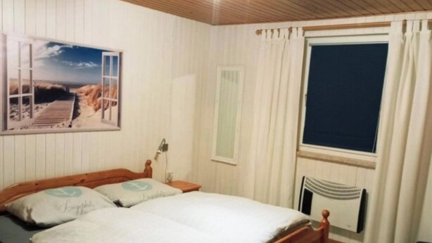 A bedroom with a bed, a nightstand, a window with curtains, and a wall-mounted picture. - Urlaub in der Natur-doppelbungalow mit Terrasse im Ferienpark Mirow (Mirow)