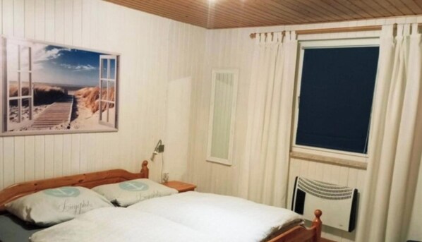 Ein Schlafzimmer mit einem Bett, einem Nachttisch, einem Fenster mit Vorhängen und einem Wandbild.