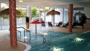 An indoor swimming pool with a central water feature, lounge chairs, and a glass-enclosed area with a view of the outside. - Urlaub in der Natur-doppelbungalow mit Terrasse im Ferienpark Mirow (Mirow)