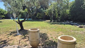 Two large, cylindrical planters in a garden area with a tree and a paved path. - A 58 m² one-bedroom ground-floor apartment, detached and adjacent to a Provençal villa (Jonquières)