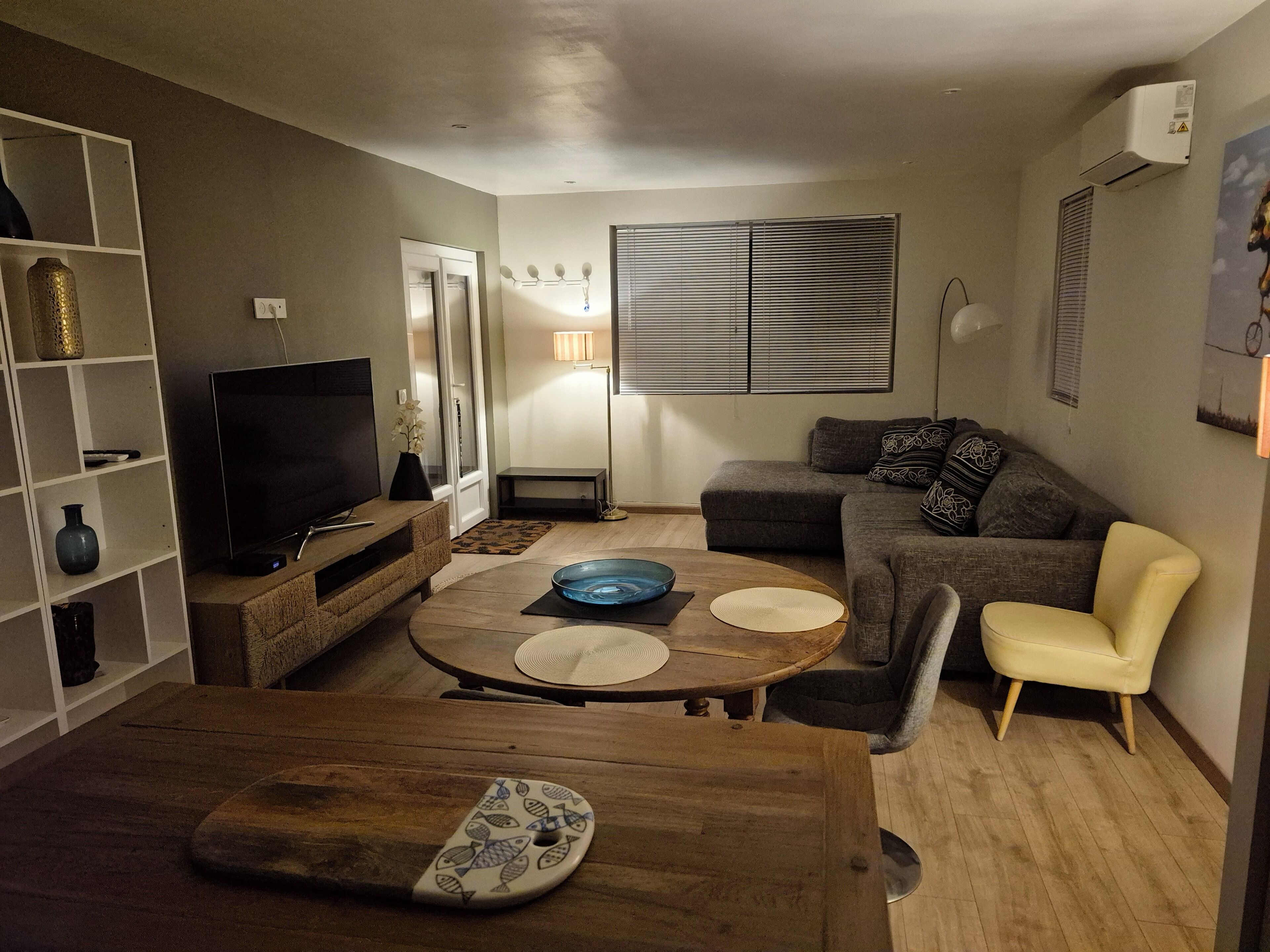 Un salon comprenant un téléviseur, un canapé, un fauteuil et une table à manger agrémentée d’un set de table à motifs de poissons.