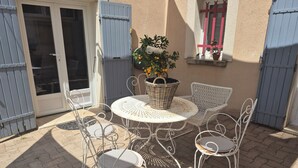 An outdoor patio with a round table, four chairs, a wicker basket, and potted plants. - A 58 m² one-bedroom ground-floor apartment, detached and adjacent to a Provençal villa (Jonquières)