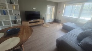 A living room with a television, a sofa, a dining table, and a bookshelf. - A 58 m² one-bedroom ground-floor apartment, detached and adjacent to a Provençal villa (Jonquières)