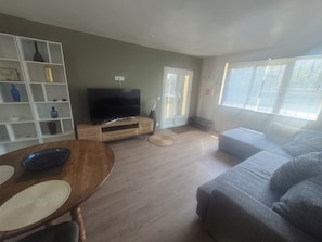 Ein Wohnzimmer mit Fernseher, einer Couch, einem Esstisch und einem Bücherregal.