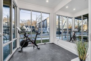A spacious room with large windows, an exercise bike, and a potted plant. - The Nash Bash | Skyline Rooftop + Mins to Downtown (Nashville)