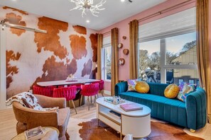 Un salon moderne avec un mur recouvert de peau de vache, un canapé turquoise, des chaises rouges et une table à manger.