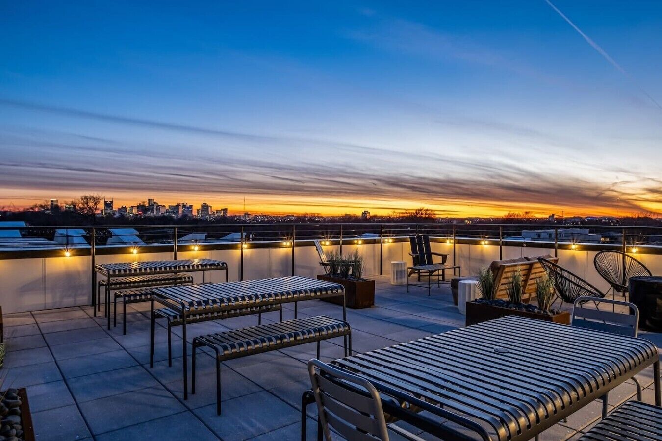 A rooftop terrace with seating and a city skyline at sunset.