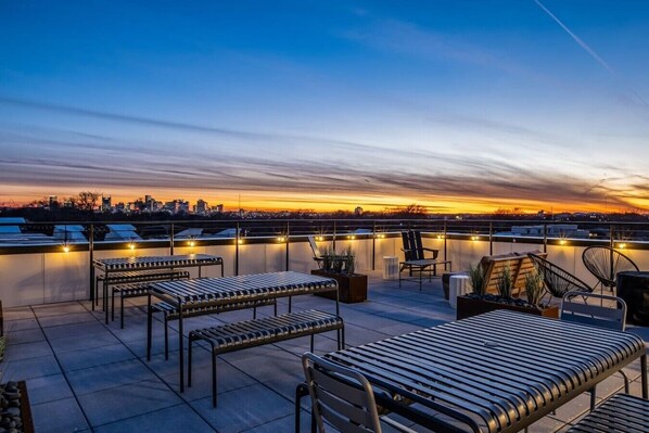 Une terrasse sur le toit, aménagée avec des sièges, offrant une vue sur le panorama urbain au coucher du soleil.