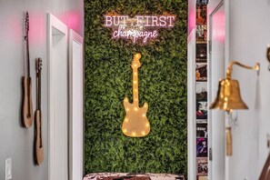 A room with a green wall, a guitar, a bell, and a neon sign that reads 'BUT FIRST champagne'. - The Nash Bash | Skyline Rooftop + Mins to Downtown (Nashville)