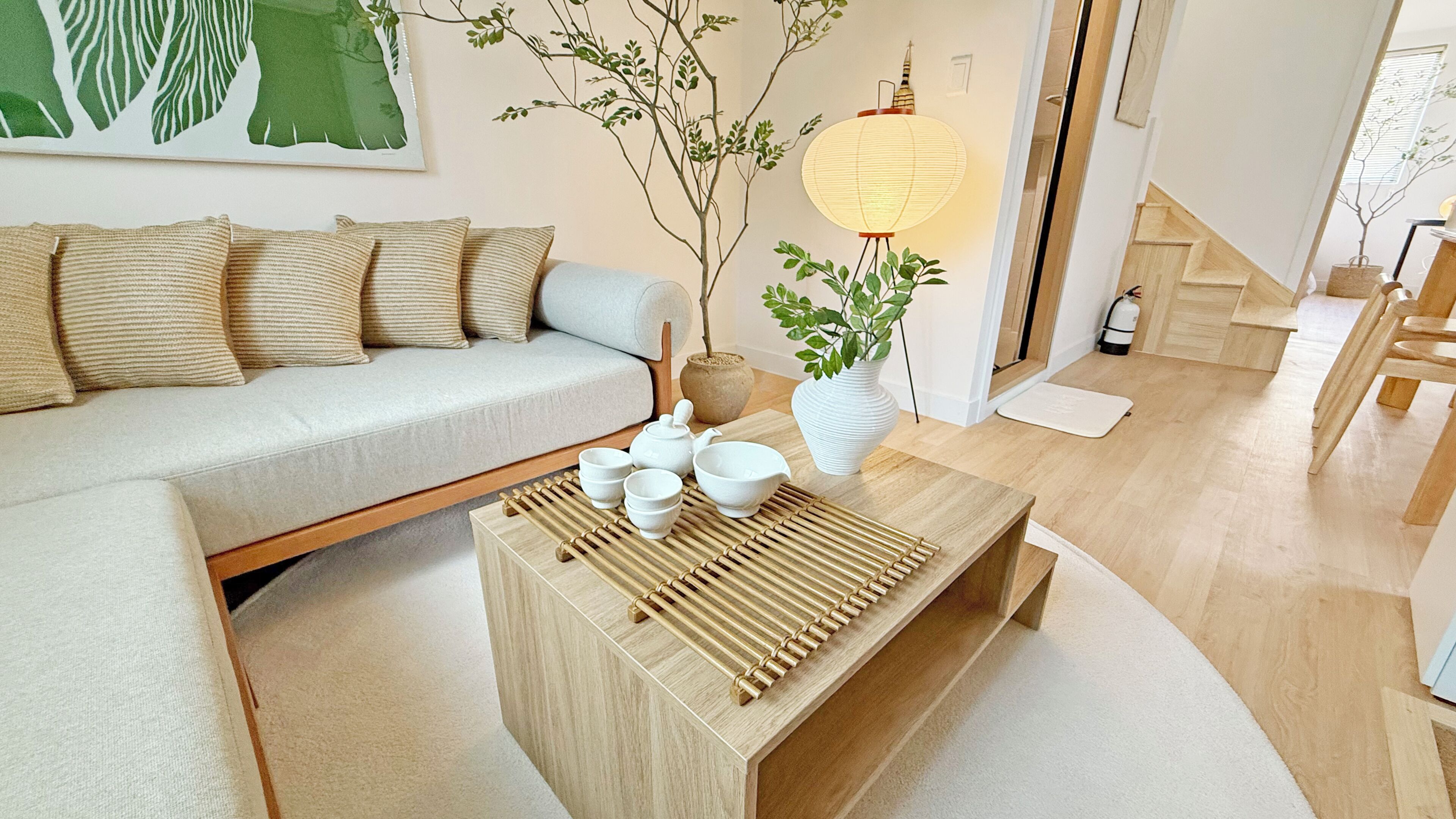A modern living room with a sofa, a coffee table with teapots, a lamp, and a staircase.