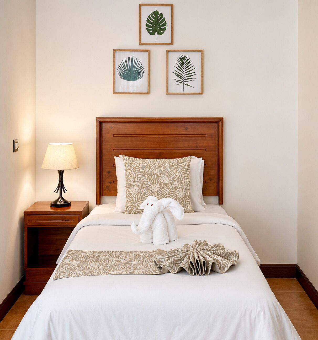 A neatly made bed with a white comforter and decorative pillows, a bedside lamp, and a plush toy on the bed.