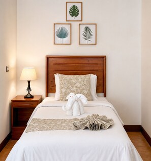 A neatly made bed with a white comforter and decorative pillows, a bedside lamp, and a plush toy on the bed. - Hotel Espadilla Gardens  (Quepos)
