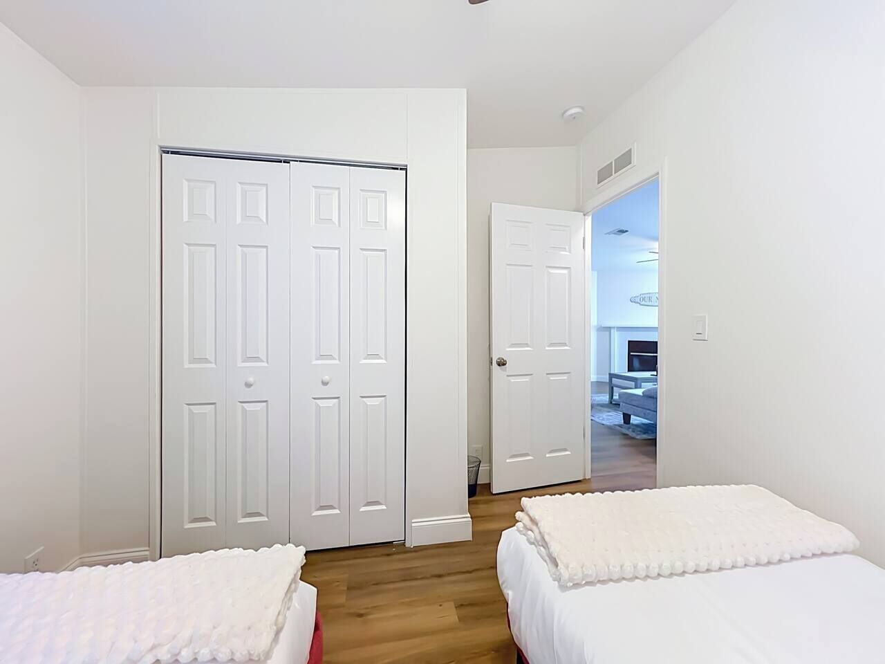 Un dormitorio con dos camas, una puerta blanca y vista a otra habitación.