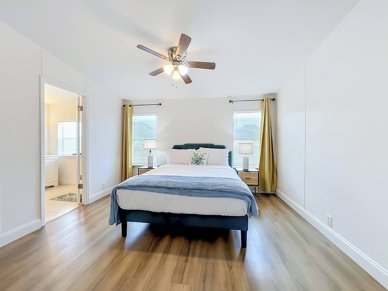 Une chambre à coucher avec un lit, un ventilateur de plafond, des lampes de chevet et une porte donnant sur une autre pièce.