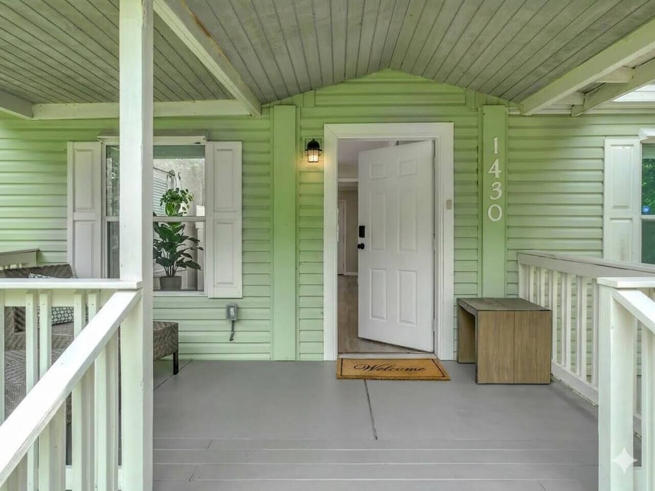 A porch with a green exterior, a white door, and a mailbox.