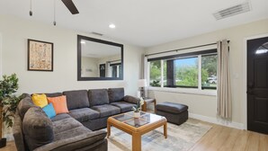 A living room with a sofa, ottoman, coffee table, and a large window with curtains. - 3-bedroom house in wonderful Winter Park with Big Fenced-In Back Yard! (Winter Park)