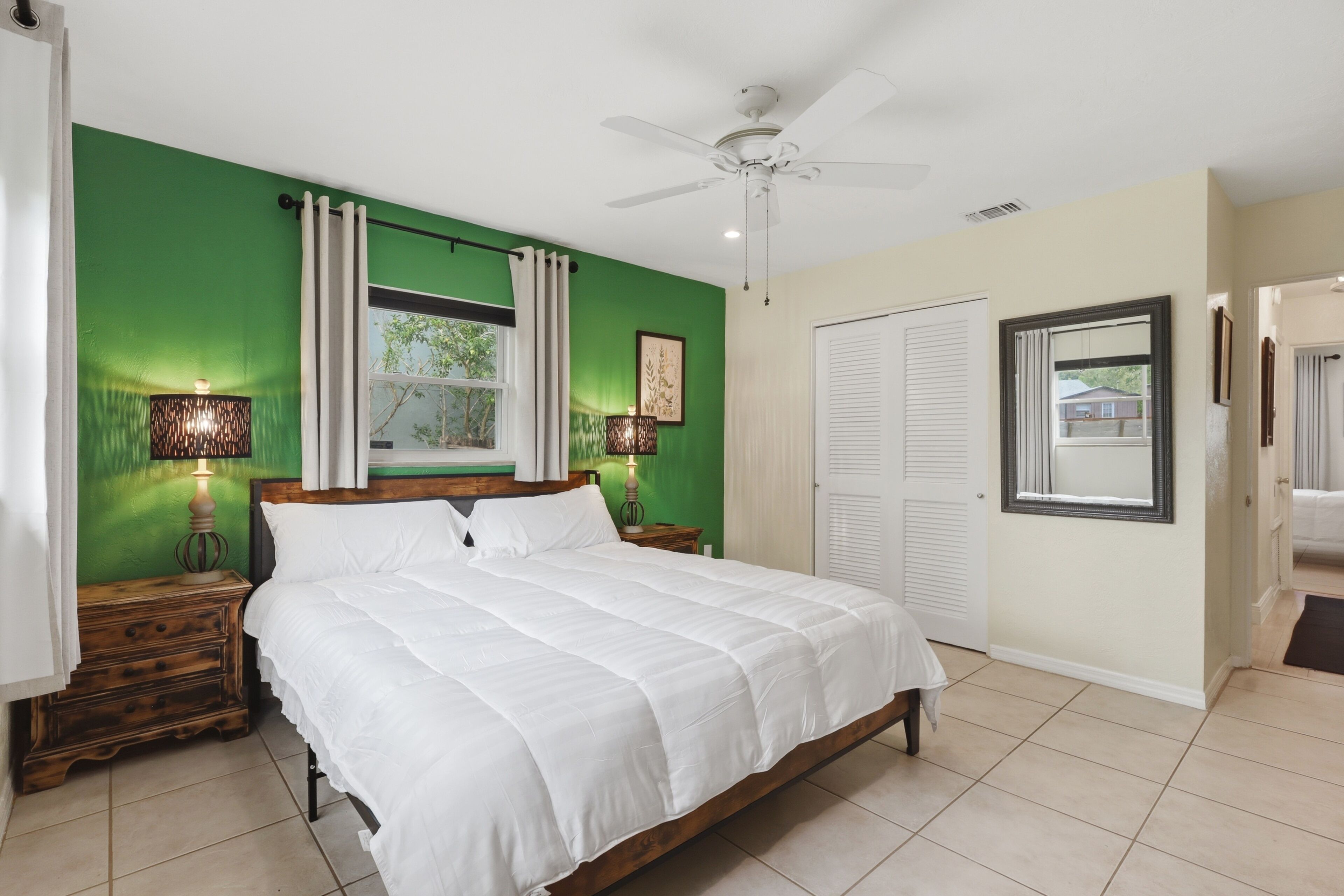 A bedroom with a bed, a ceiling fan, a window with curtains, and a door.
