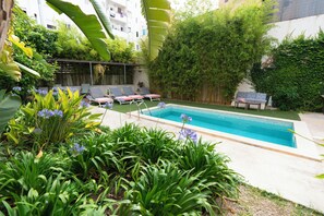 En swimmingpool med liggestole og en have med forskellige planter.