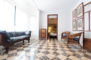 Et værelse med et mønstret gulv, en sofa, to fletstole og en seng med et natbord.