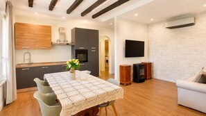 Una cocina moderna con electrodomésticos integrados, un comedor con una mesa lista para dos personas y una sala de estar con sofá y televisor de pantalla plana.