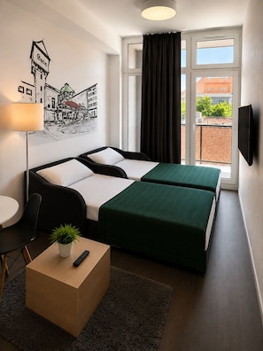 Ein Hotelzimmer mit Bett, Schreibtisch, Stuhl, Fernseher, einem Fenster mit Vorhängen und einem Wandbild.