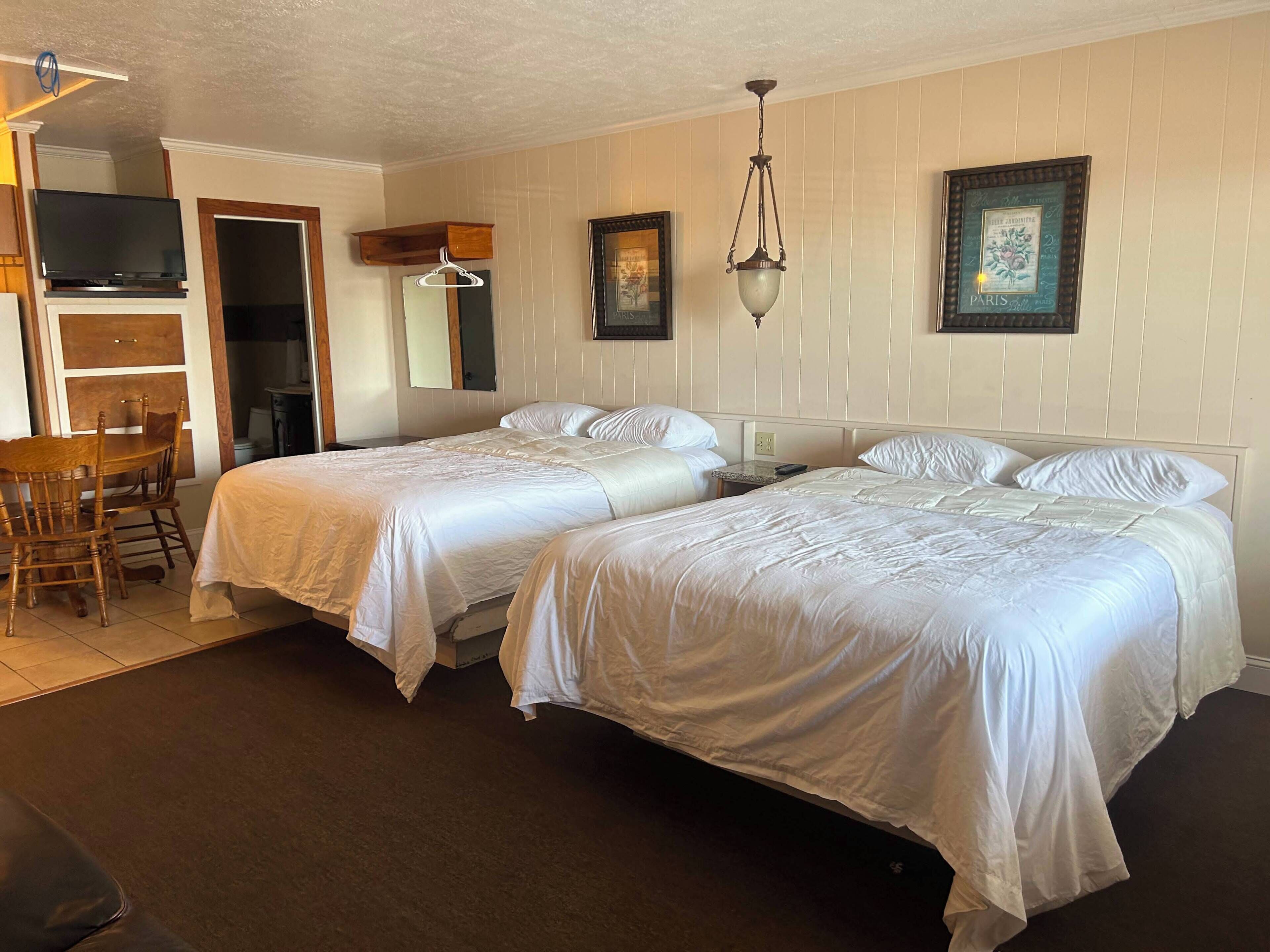 A hotel room with two beds, a desk with a chair, a television, and a framed picture on the wall.