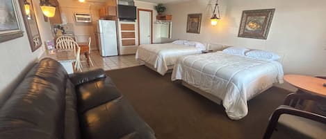 Ein Hotelzimmer mit einer schwarzen Ledersofa, zwei Einzelbetten, einem kleinen Tisch, einem Kühlschrank und einem Fernseher.