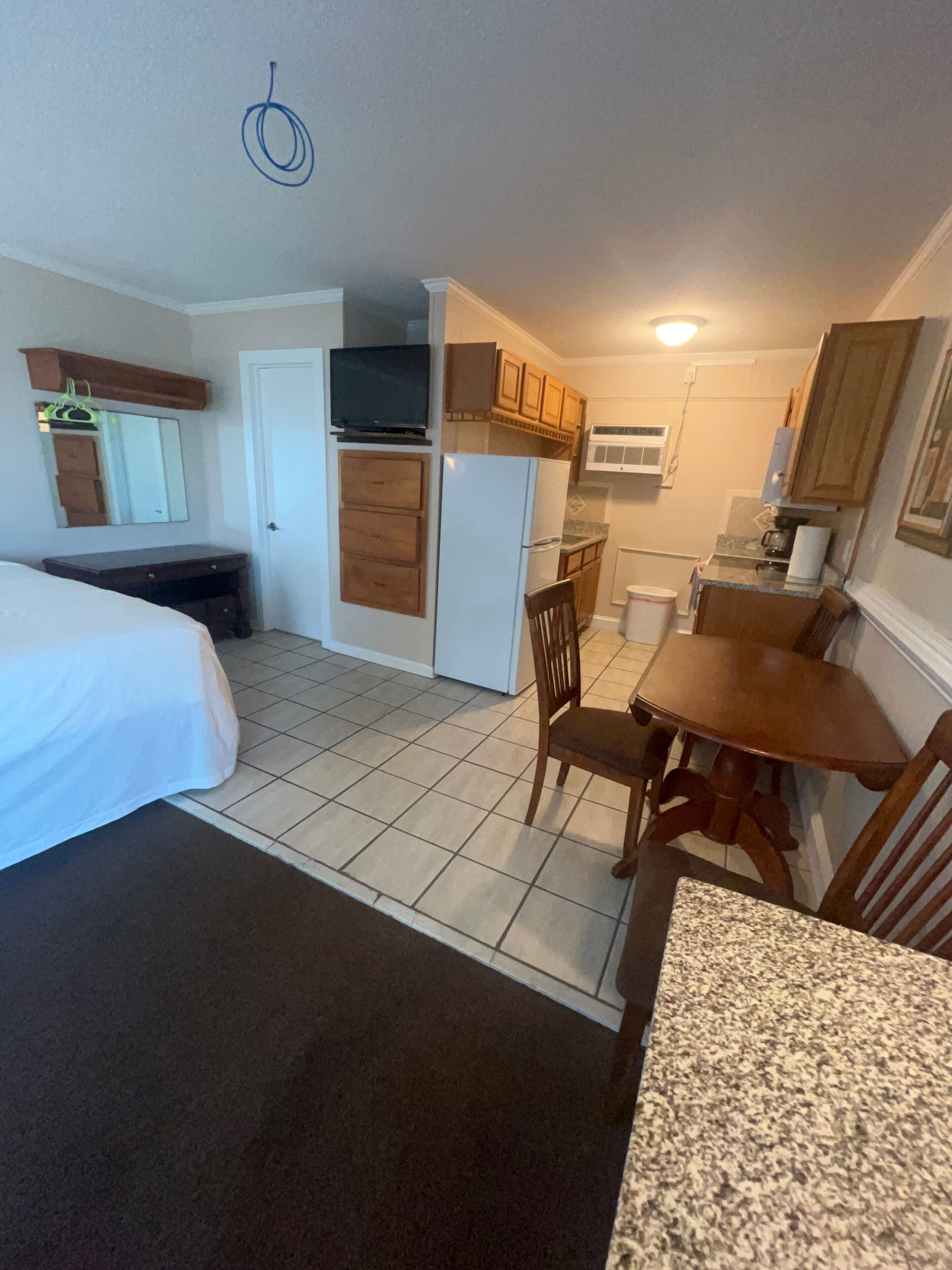 A compact hotel room with a bed, a small kitchenette, a dining area with a table and chairs, and a mirror.