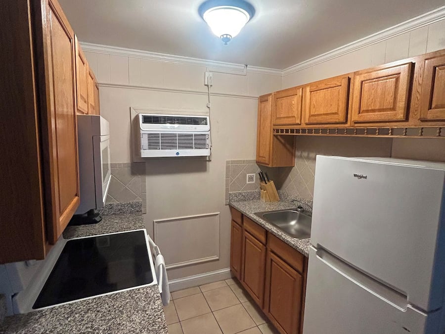 Una cocina compacta con armarios de madera, estufa integrada, refrigerador y unidad de aire acondicionado.