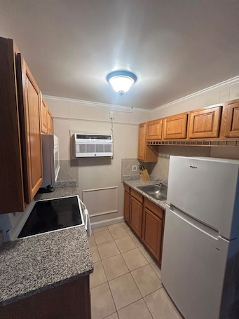 A compact kitchen with wooden cabinets, a built-in stove, a refrigerator, and an air conditioning unit.